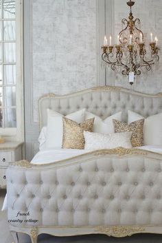 a white bed with gold pillows and chandelier