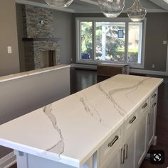 an empty kitchen with marble counter tops and island in front of the fireplace, is shown