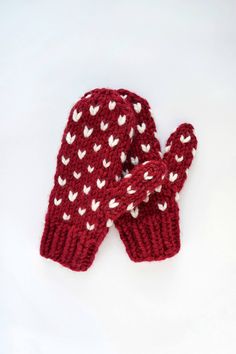 two red mittens with white hearts are on a white surface and one is in the shape of a heart