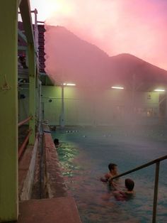 two children playing in an outdoor swimming pool at night with the sun setting behind them