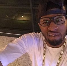 a man with glasses and a chain around his neck is posing for the camera while wearing a white t - shirt