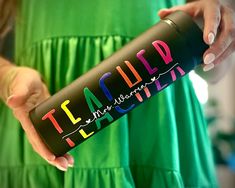 a woman holding a black water bottle with the word team wild painted on it in pink, blue, and green