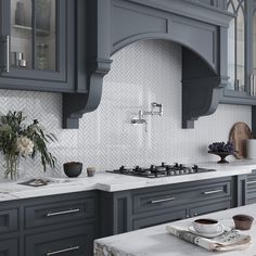 a kitchen with gray cabinets and marble counter tops, along with a white tiled backsplash