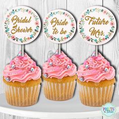 three cupcakes with pink frosting and flowers on top, sitting on a shelf