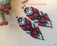 two red and black beaded earrings sitting on top of a wooden table next to flowers