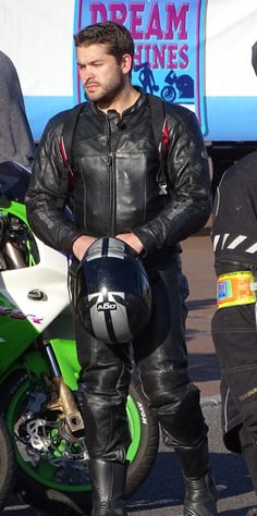 a man standing next to a motorcycle on a street with other people around him and another person in the background