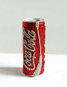 a soda can covered in red and silver sequins sitting on a white surface