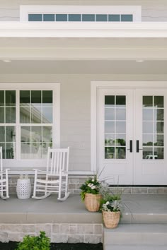 two white rocking chairs sitting on the front steps of a house with potted plants