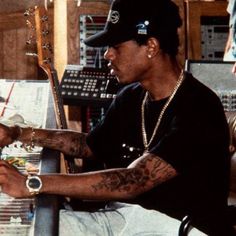 a man sitting in front of a mixing desk with headphones on his ears and wearing a baseball cap