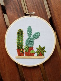 a cross stitched cactus with potted plants on a wooden chair in front of a fence