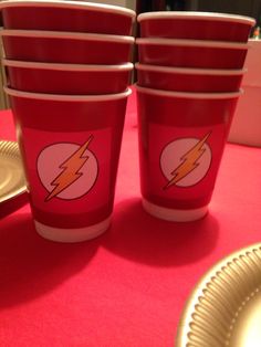 red cups with the flash logo on them are sitting on a table next to gold plates