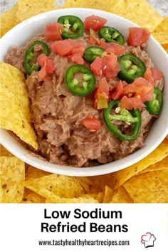 a white bowl filled with refried beans surrounded by tortilla chips and jalapenos