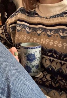 a woman holding a coffee cup in her hand while sitting on the floor next to someone's leg