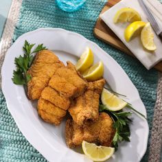 a white plate topped with fried fish next to lemon wedges