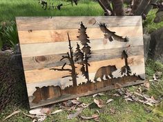 a wooden sign with bears and trees on it sitting in the grass next to a tree