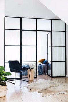 a room with a chair, bed and plants in it on the floor next to a window