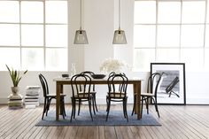 a dining room table with four chairs and a vase on the table in front of two windows