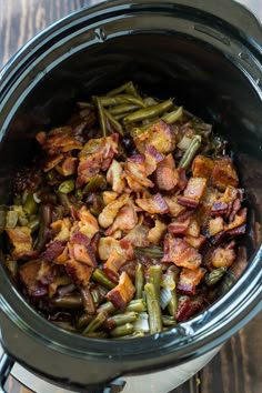 a crock pot filled with green beans, bacon and other toppings on top of a wooden table