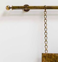 an antique brass clock hanging from a chain on a wall with a white background and gold accents