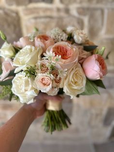 a person holding a bouquet of flowers in front of a brick wall with white and pink flowers