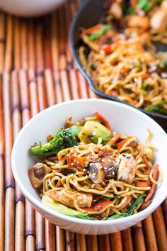 a white bowl filled with noodles and vegetables on top of a bamboo mat next to a skillet