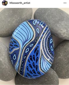 a blue and white painted rock sitting on top of some gray rocks with black dots