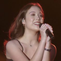 a woman holding a microphone in her right hand and smiling at the camera while she sings