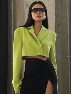 a woman in a lime green jacket and black skirt with sunglasses on her head standing next to a wall