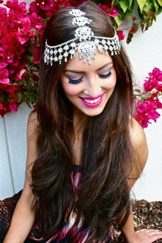 a woman with long hair wearing a tiara and smiling at the camera while sitting in front of flowers