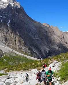 three people hiking up the side of a mountain in front of some snow capped mountains