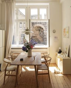 a dining room table with chairs and a vase filled with flowers sitting on top of it