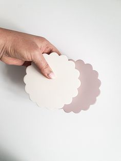 a person's hand holding three white scalloped coasters