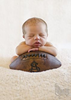 a baby laying on top of a football with his head resting on it's hands