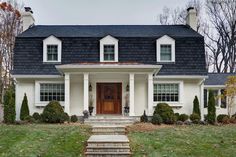 a white house with black shingled roof and two story entryway leading up to the front door