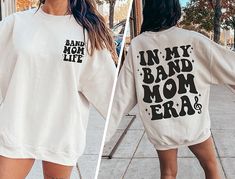 "✦ 🇺🇸SENT TO PRODUCTION AND PRINTED IN THE US🇺🇸 ✦The perfect In My Band Mom Era Graphic Crewneck Sweatshirt is yours!  ✦ QUICK FACTS ✦ Gildan 18000 Crewneck Sweatshirt is 50% cotton, 50% polyester preshrunk fleece *Heather Colors are 40% cotton, 60% polyester ✦ SIZING TIPS ✦ All our garments are UNISEX.  FOR AN OVERSIZED LOOK, SIZE UP 2-3 SIZES For a Relaxed Fit order your Usual Size For a Snug Fit order 1 Size down If you're unsure: Lay your favorite fitting Crewneck Sweatshirt flat and *measure armpit to armpit (1\" under armpit) for width *measure from point where neck seam meets shoulder all the way to bottom for length & compare with measurements in Size Chart provided in each listing *Please note, Size Chart Measurements are to be used as guidelines and measurements may vary with Music-themed White Tops With Letter Print, Cotton Band Merch Short Sleeve Sweatshirt, Music-themed White Crew Neck Top, Cotton Short Sleeve Sweatshirt Band Merch, White Long Sleeve Top For Concert, Music-themed White Relaxed Fit Top, Music-themed Cotton Sweatshirt With Letter Print, Music-themed Long Sleeve Cotton Top, Long Sleeve Cotton Tops With Band Logo