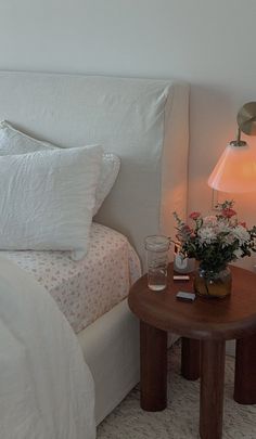 a bed with white linens and pink flowers on the night stand next to it