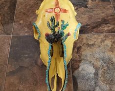 a yellow cow skull with cactus decorations on it's head sitting on a tile floor