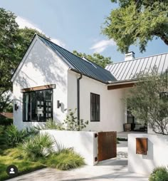 a white house with a metal roof and wooden doors on the front door is surrounded by greenery