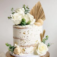 a white wedding cake with flowers and leaves on top is sitting on a wooden stand