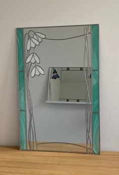 a mirror sitting on top of a wooden table next to a white vase with flowers