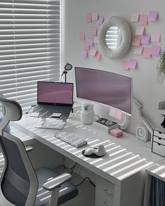 a white desk topped with two computers next to a window covered in pink sticky notes