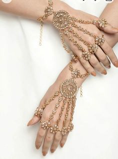 a woman's hands with gold jewelry on them and her hand in the middle