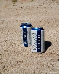 two cans of beer sitting in the sand