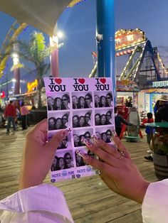 a woman holding up some pictures with the words i love you on them in front of an amusement park