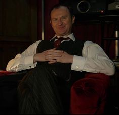 a man in a vest and tie sitting on a red chair