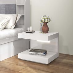 a white table with a book and vase on it next to a bed in a bedroom