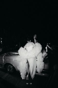 an old car with white feathers on it and a man in a suit standing next to it