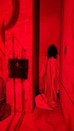 a woman in a red light room with her back turned to the camera, looking down