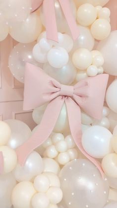 a bunch of white balloons with a pink bow on it and some other balloons in the background