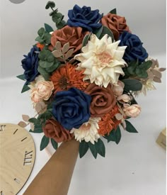 a bridal bouquet with blue, orange and white flowers on it next to a clock